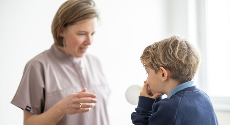 Frau Dr. Beckmann steht gegenüber eines Jungen, der einen Luftballon aufbläst.